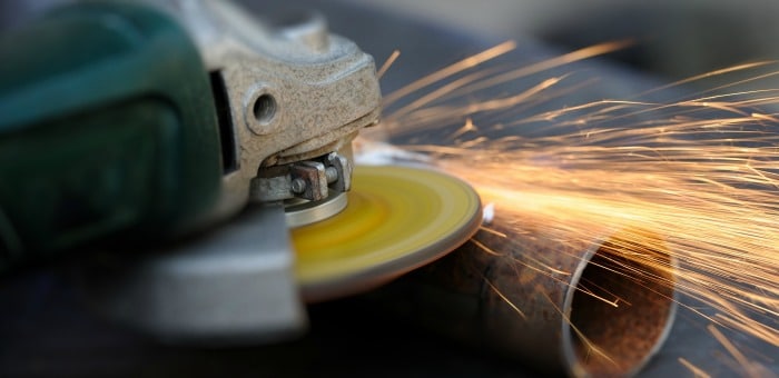 A right angle grinder in use on a copper pipe with sparks flying