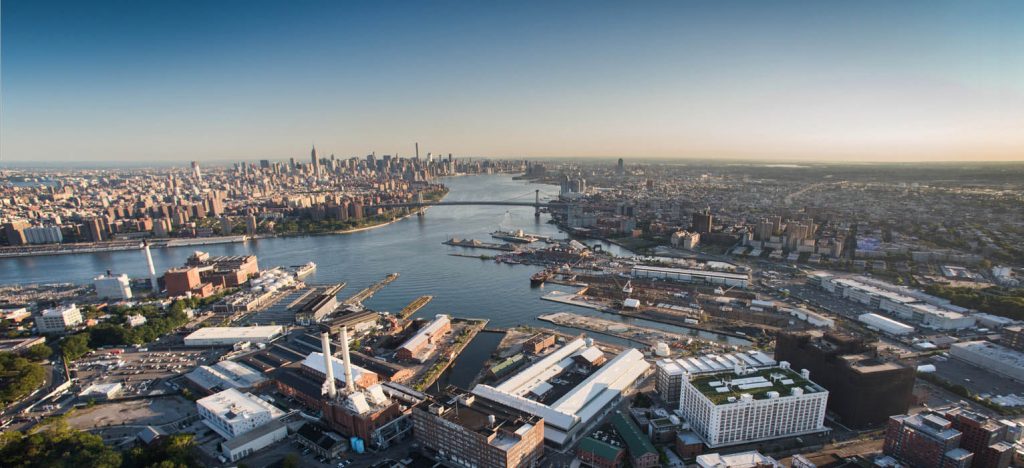 Aerial color image of the Brooklyn Navy Yard looking up the East River with a daytime Manhattan skyline