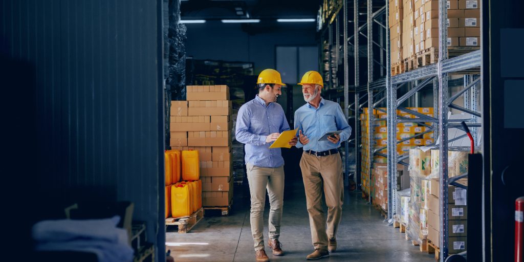 Two workers walking side by side in hard hats in a warehouse