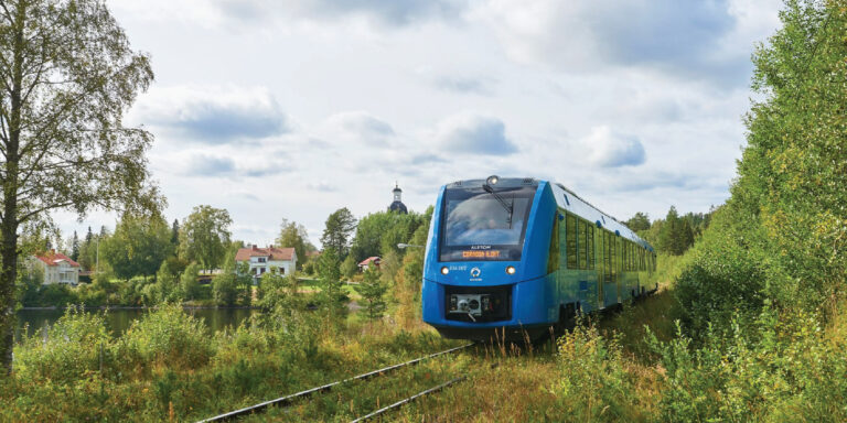 Alstom Commuter train on rural track near a pond and small town with white buildings