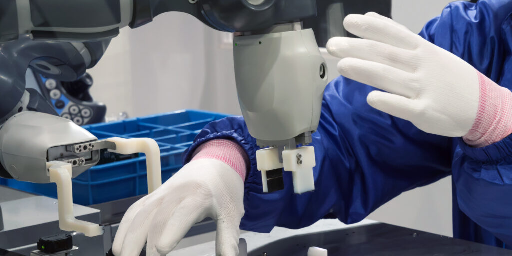 Worker in a lab wearing gloves adjusting a robot with a grabber arm