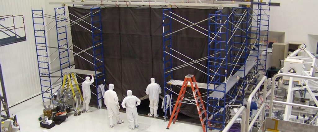 Workers near scaffolding wearing white PPE garments.