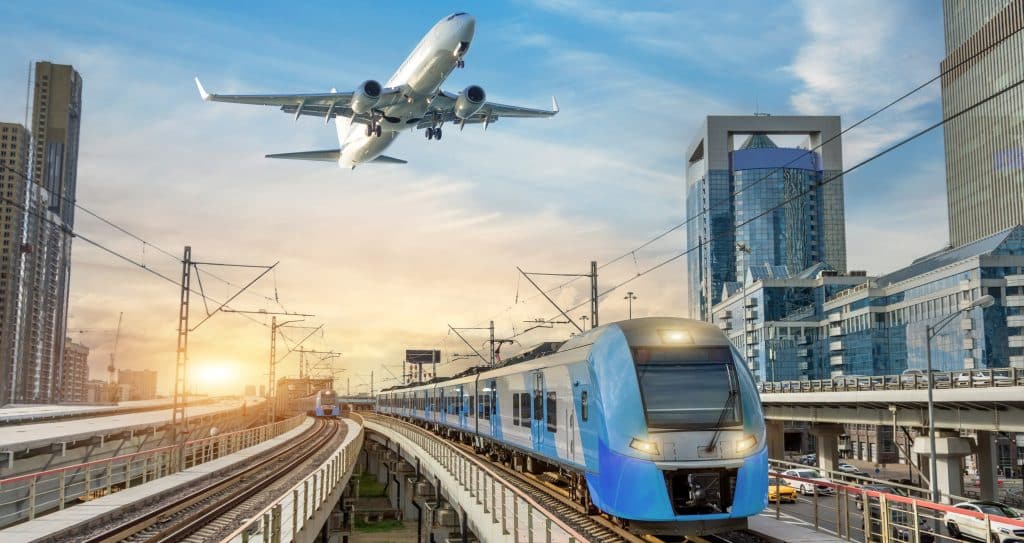 Urban view of railway tracks and suburban electric trains rushing along among high rise buildings. Passenger plane flying in sky, landing at airport. Concept of modern infrastructure transport travel.